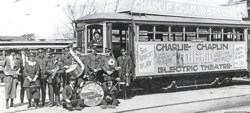 Old black and white photo of men in front of a Charlie Chaplin, Electric Theatre bus